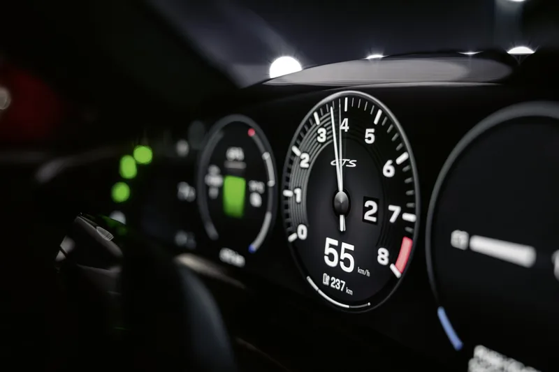 Přístrojový štít Taycanu GTS v šeru: kulatý ukazatel s číselnou stupnicí a nápisem GTS ukazuje 55 km/h a dojezd 237 km, vlevo vedle něj zelené sloupce ukazatele energie.