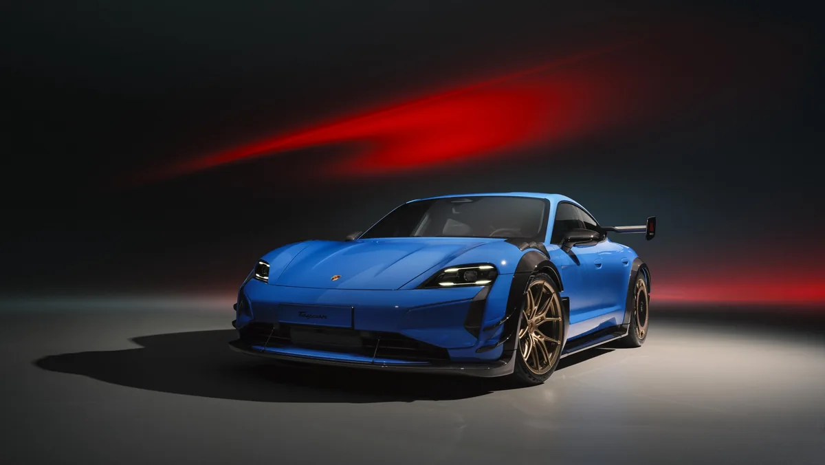 Modrý Taycan Turbo GT s Manthey Kitem ve studiu, zepředu zleva; vysoké zadní křídlo, bronzová kola, za vozem červený pruh světla na tmavém pozadí.